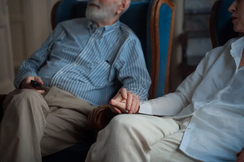 A married couple holding hands in their armchairs in the evening