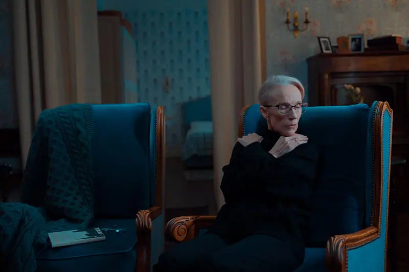 A resident in a dark sweater resting in a blue velvet armchair in the parlor