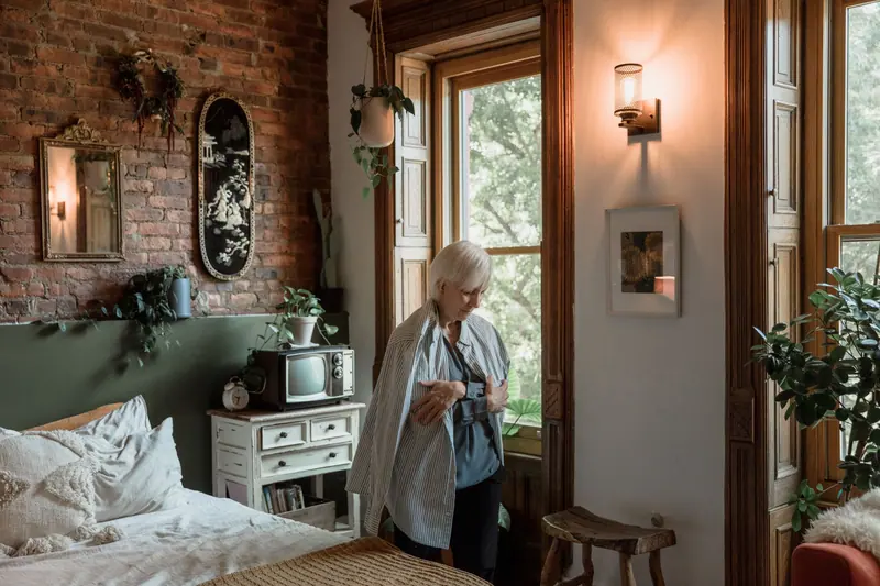 A resident in her room by lamplight, among her plants and pictures