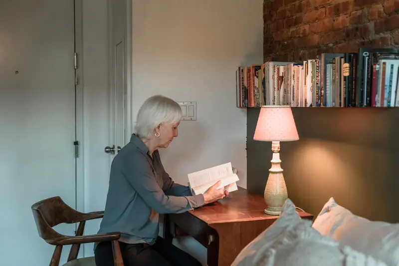A resident reading at her writing desk under a pink-shaded lamp