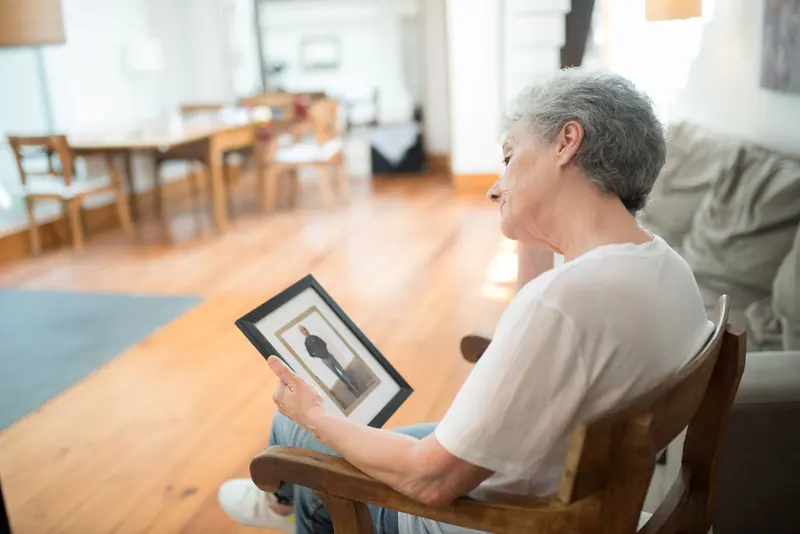 A resident in the sitting room holding a framed photograph of her husband