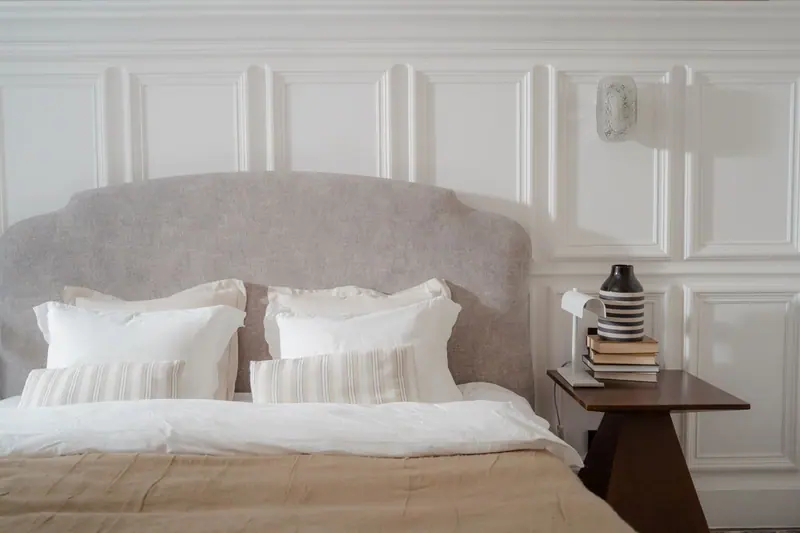 Elegant bedroom with cozy bed and stylish side table. Features neutral tones and soft lighting.