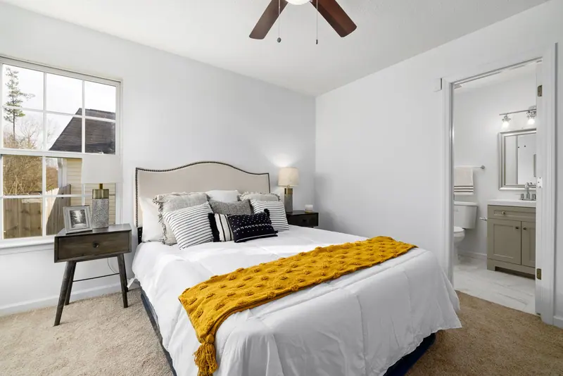 Modern bedroom design featuring a cozy bed, ceiling fan, and bright natural light through a large window.