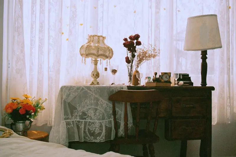 A vintage writing desk with lamps and roses by a lace curtain