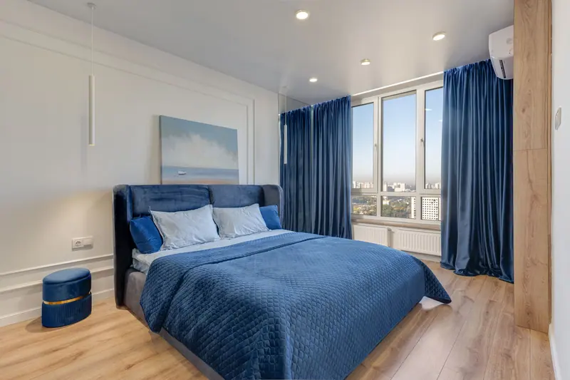 A stylish bedroom with blue decor and large windows offering a city view.