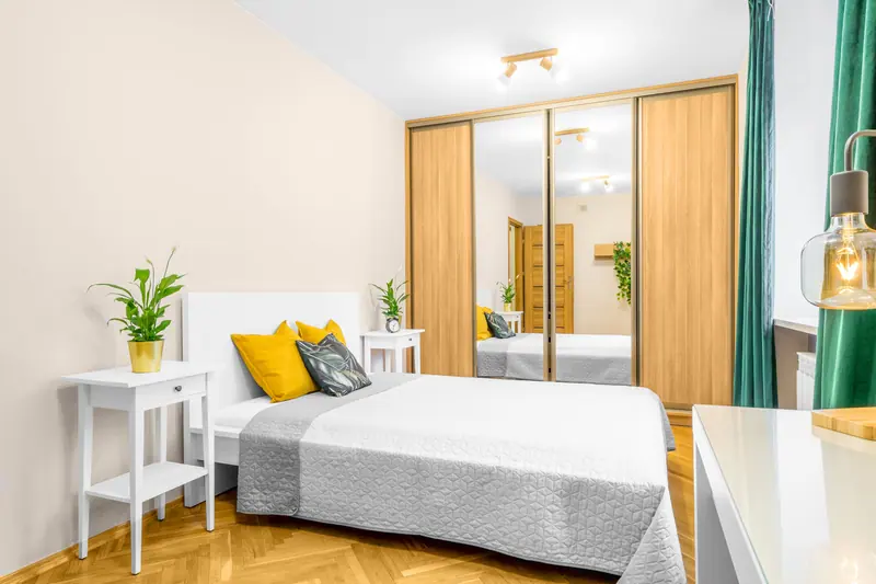 Bright and cozy modern bedroom interior with mirrored wardrobe and vibrant accents.