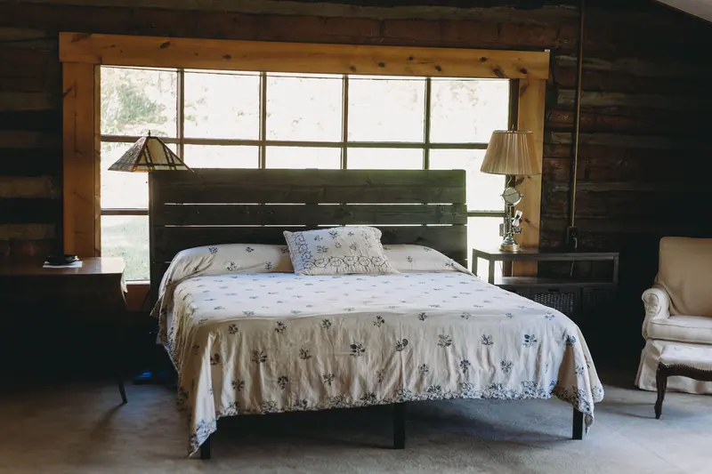 Cozy rustic bedroom featuring natural wood elements, large window, and a comfortable bed.