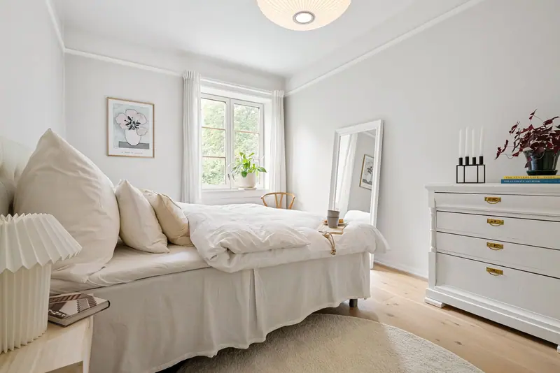 Elegant minimalist bedroom with white bedding, plants, and natural light