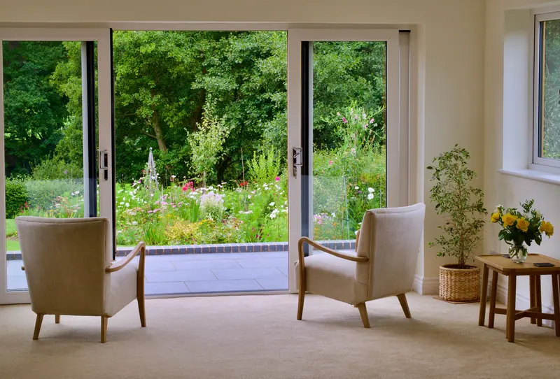 French doors open from a garden cottage sitting room onto the flower beds