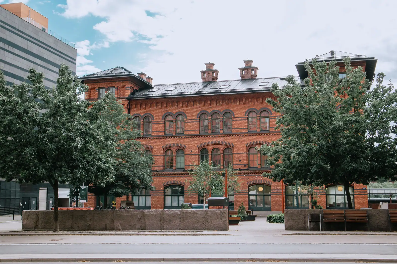 The red brick Old Main hall with arched windows and chimneys, framed by shade trees