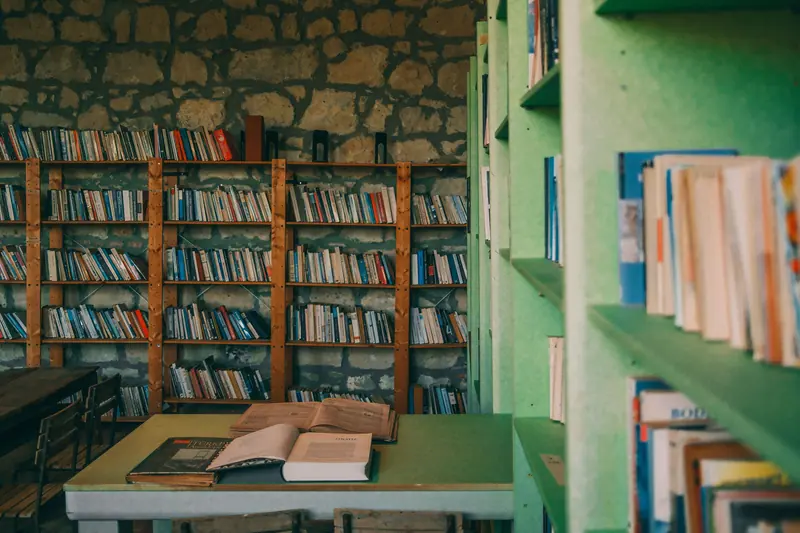 Shelves of books and an open volume on the library's green reading table