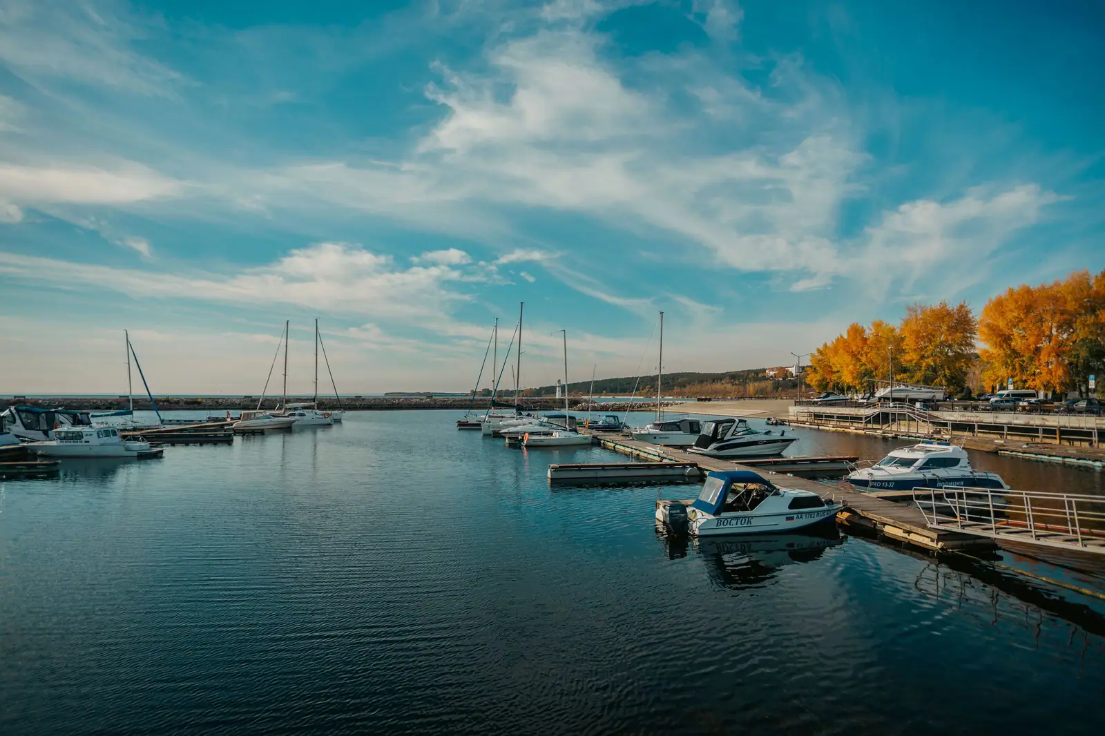 Idyllic marina scene with boats docked by vibrant autumn trees under a bright sky.