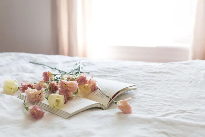 A serene bedroom scene with fresh flowers on an open book, epitomizing tranquility and elegance.