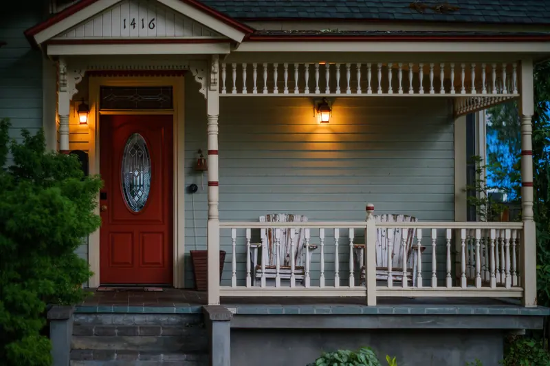 A porch with a red door and lights glowing at dusk