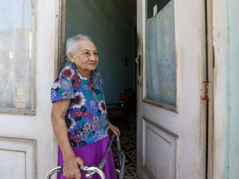 A former patient smiling at her own front door with her walker