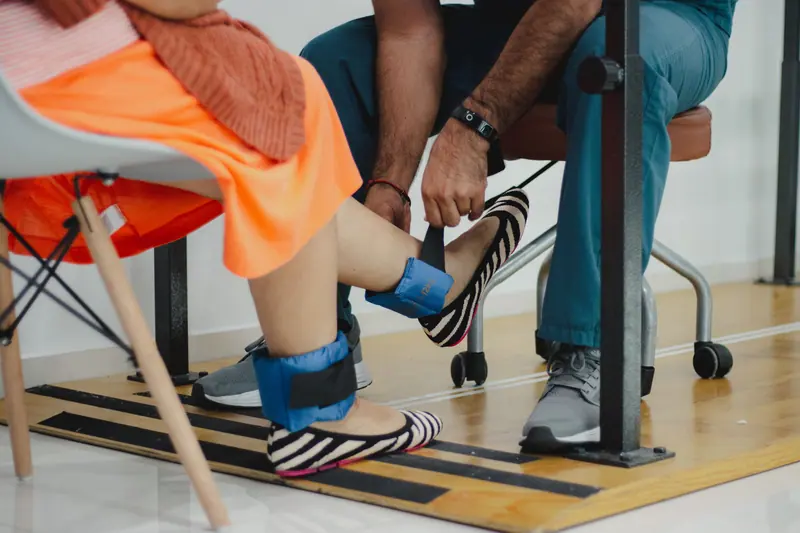 A therapist fitting ankle weights for a seated leg-strength exercise