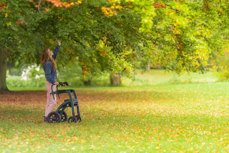 A patient practicing outdoor walking with her rollator on the autumn path
