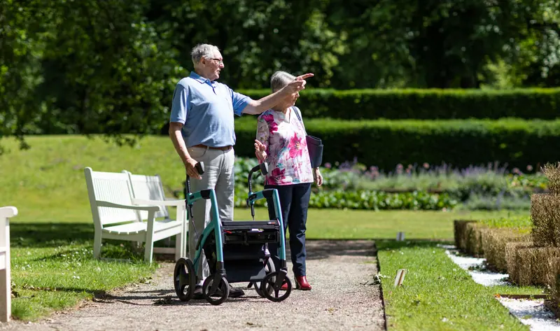 A guest walking the garden path with her rollator and her husband