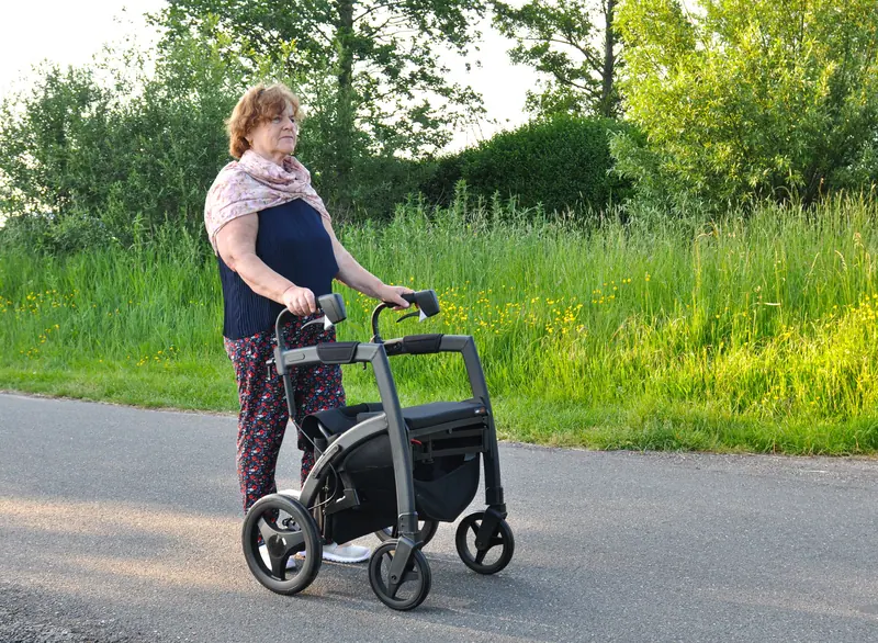 A woman walking a country lane with her rollator