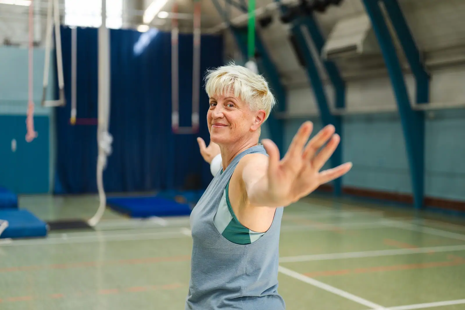 A patient smiling as she stretches her arm out during a session in the therapy gym