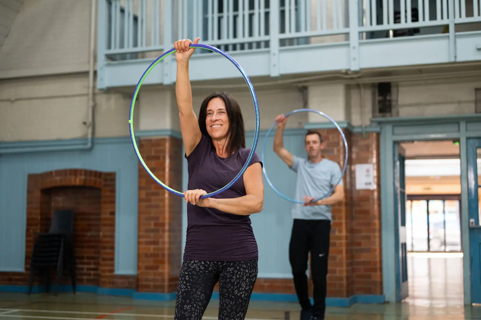A patient laughing as she spins a hula hoop during group exercise class, her therapist joining in behind her