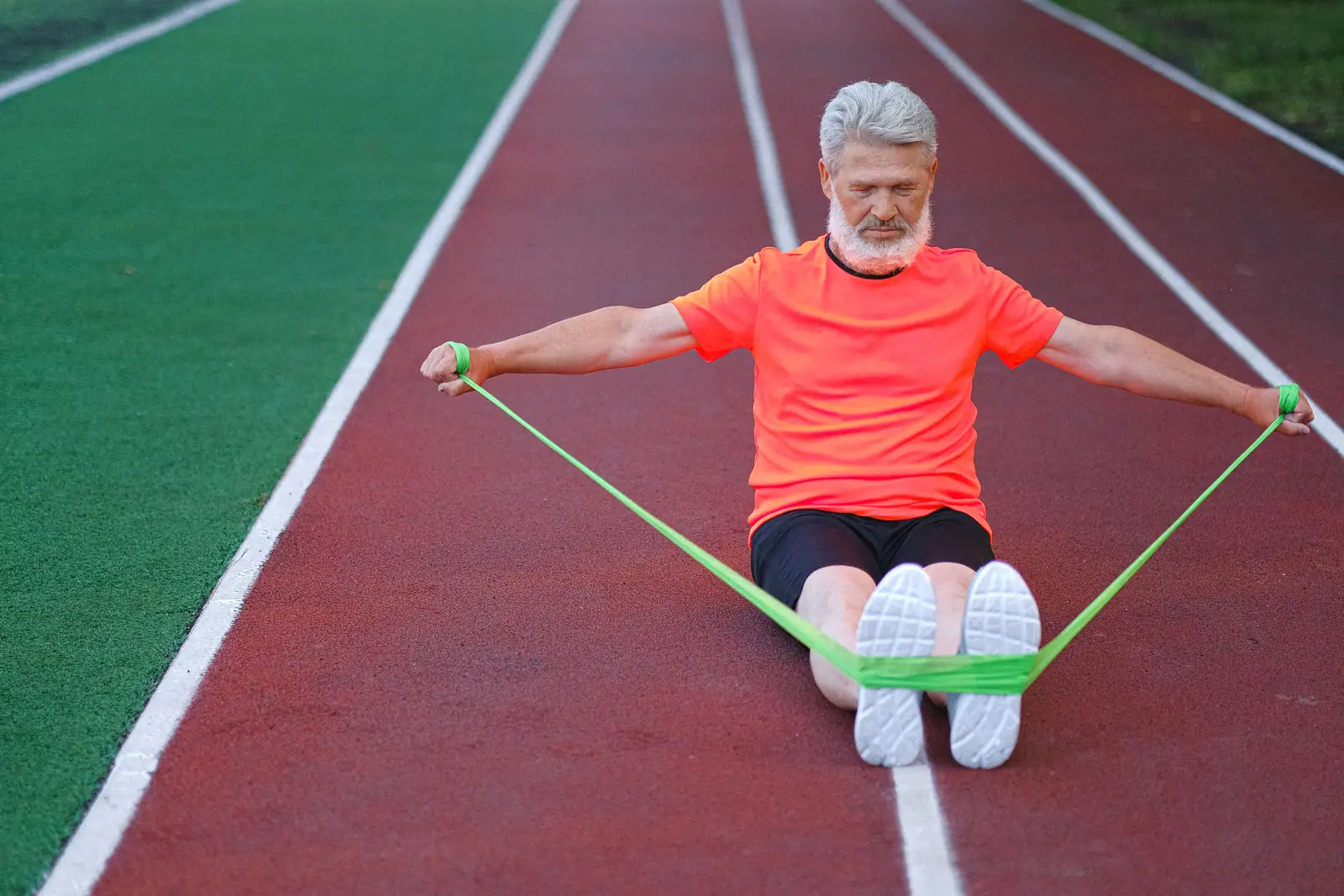 A patient doing a seated resistance-band row on the running track behind the therapy gym