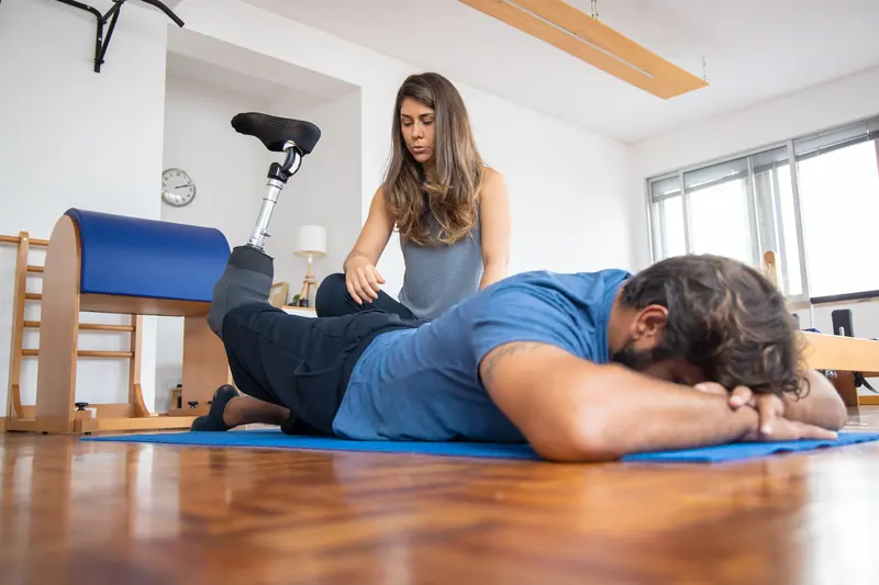 A therapist helping a patient with a prosthetic leg through floor exercises