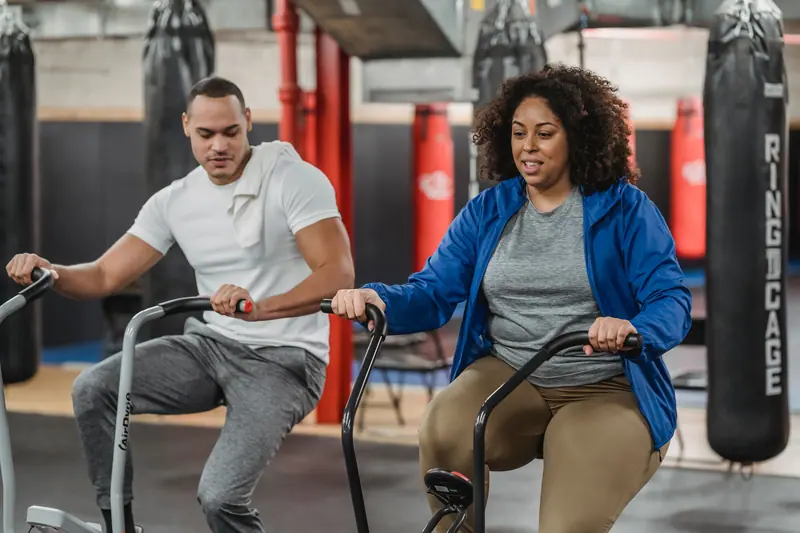 Two patients pedaling stationary bikes side by side in the therapy gym