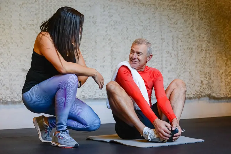 A therapist crouching beside a patient on the mat as he stretches