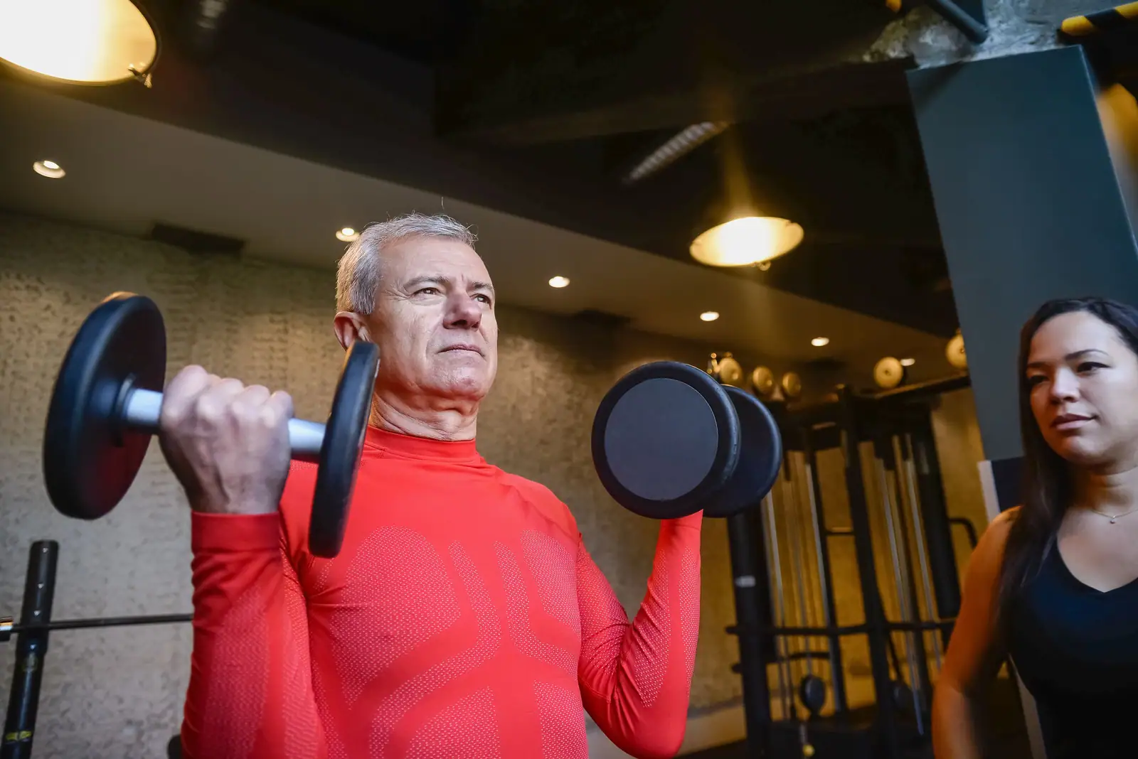 A patient curling dumbbells as his therapist watches his form in the therapy gym