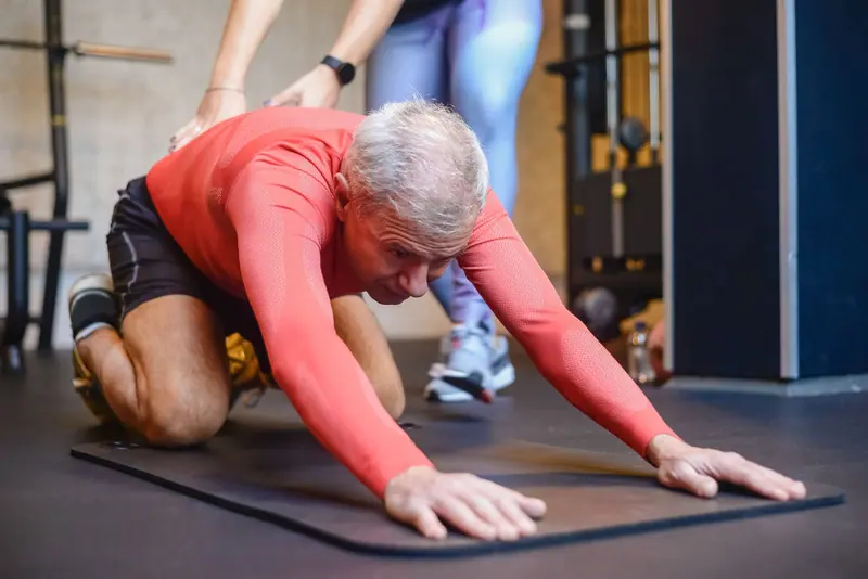 A patient stretching on a mat with his therapist's help
