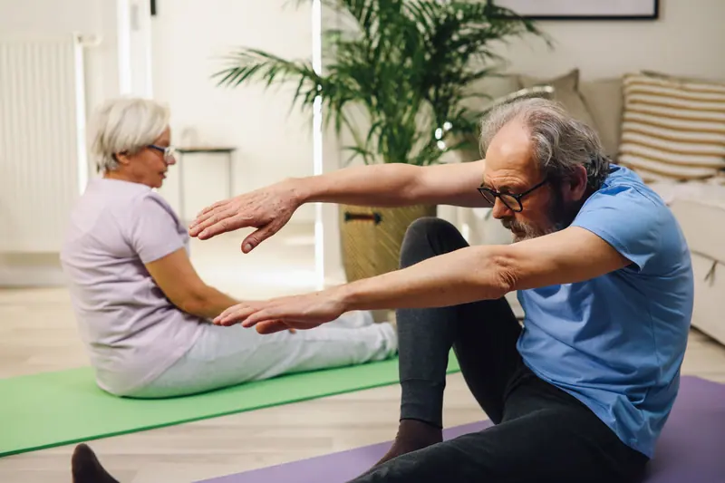 An older couple stretching together on mats at home