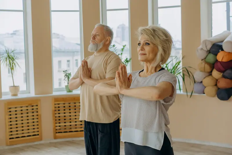 Two guests doing gentle stretches by the sunny windows