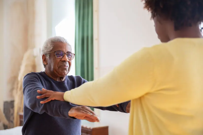 A therapist guiding a resident through arm exercises by the window