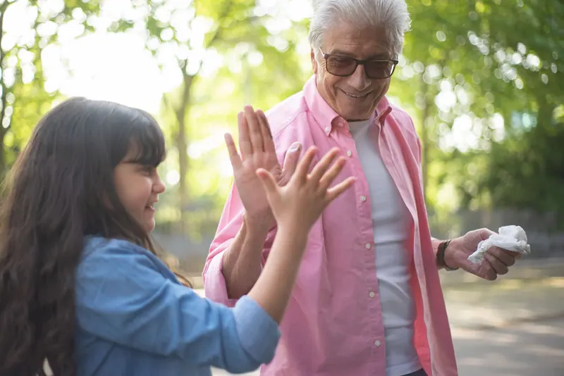 A grandfather giving his granddaughter a high five in the park