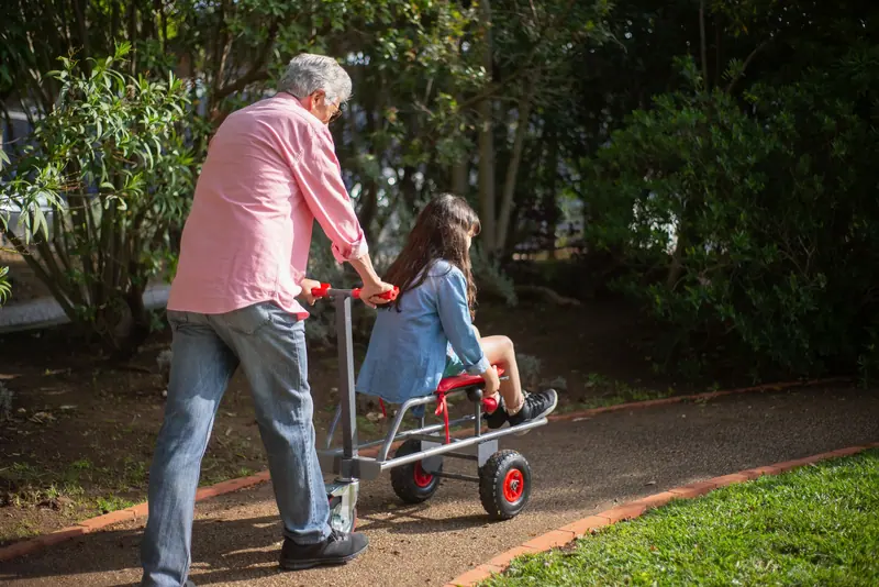 A grandfather pushing his granddaughter in a cart through the park