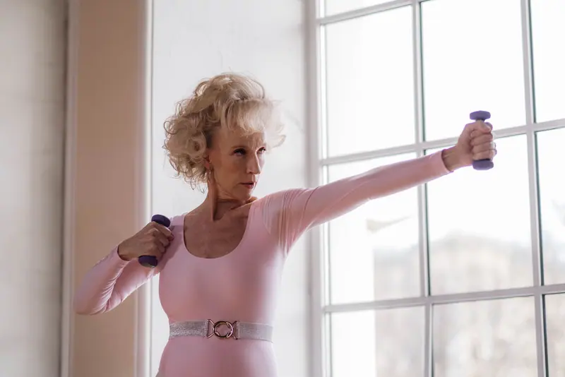 A patient lifting light hand weights by the big gym windows