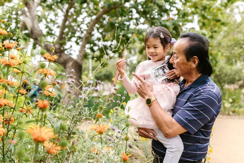 A grandfather carrying his granddaughter through the garden