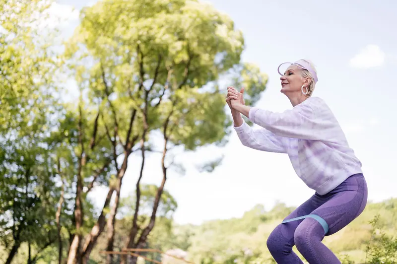 A woman doing squats outdoors with a resistance band