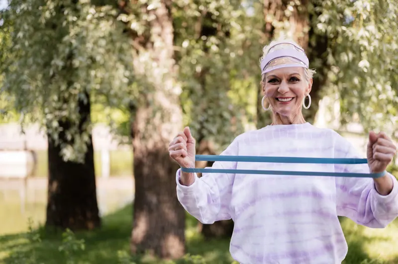 A woman smiling with her resistance band under the trees