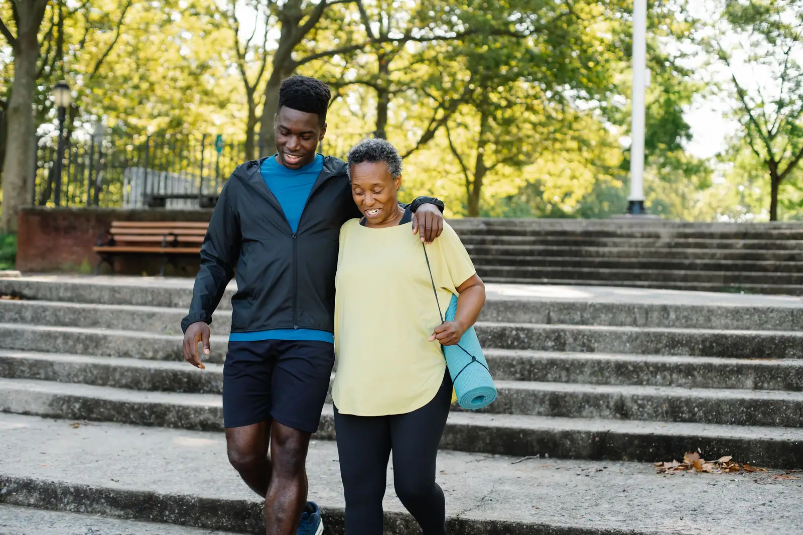 A mother and her grown son walking together along a shaded park path after a morning workout
