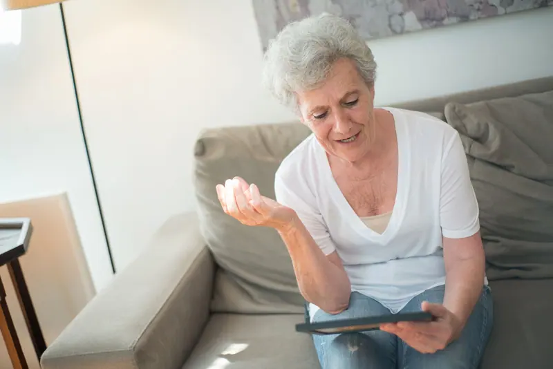 An older woman smiling during a video call on her couch