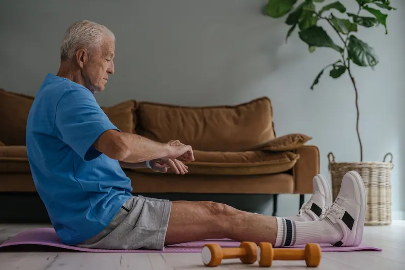 An older man stretching on a mat in his living room