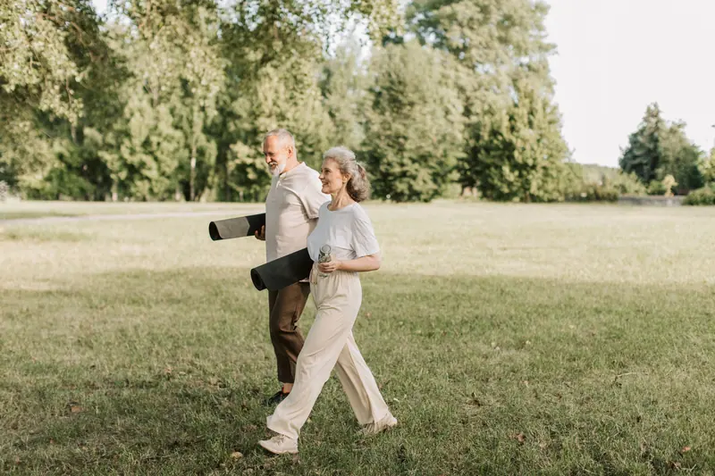 An older couple walking across a park lawn with yoga mats