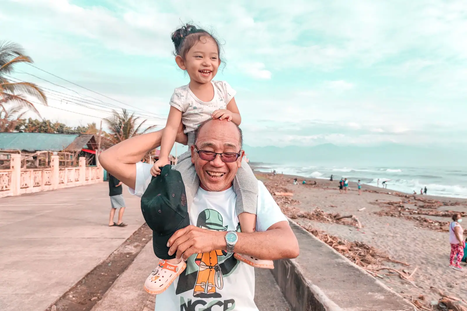 A grandfather laughing as he carries his granddaughter on his shoulders along the seawall