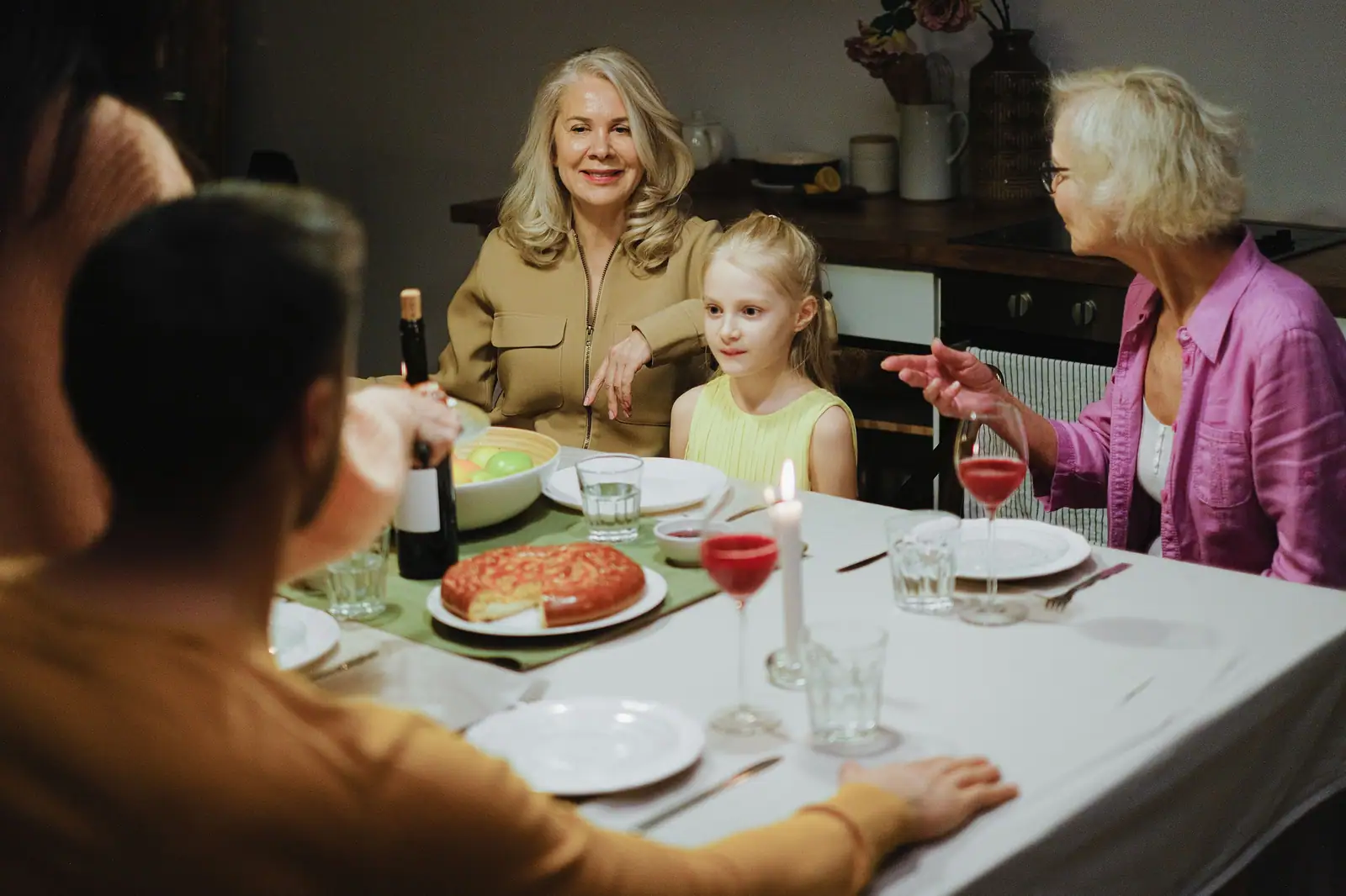 A resident in a pink cardigan laughing with her family around the dinner table