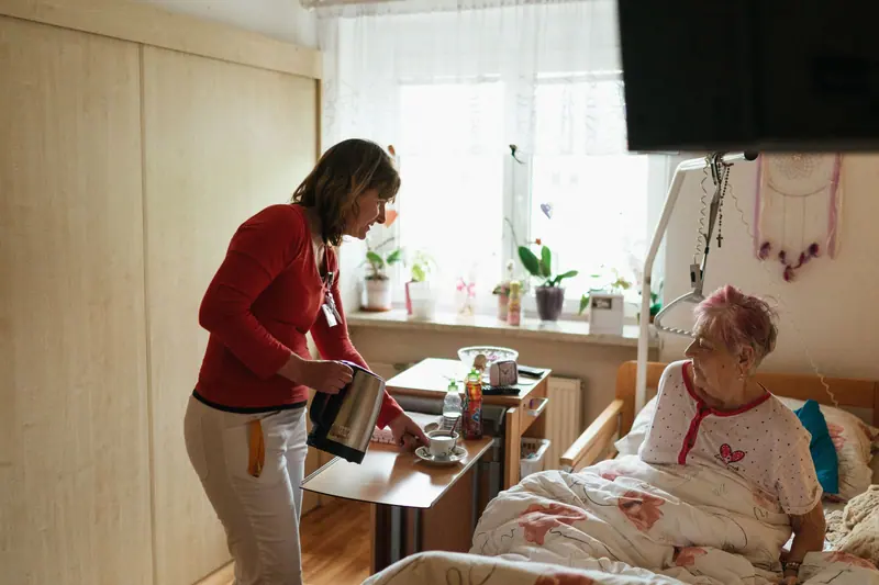 A caregiver bringing tea to a resident in her bright bedroom