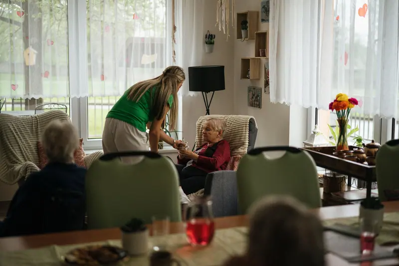 A caregiver pouring tea for two residents in the sunny sitting room