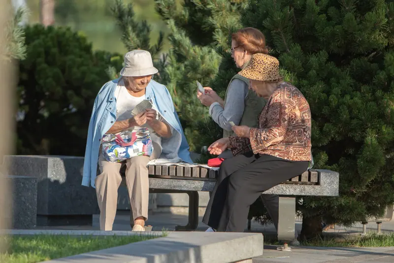 Two residents playing cards on a garden bench in the sunshine