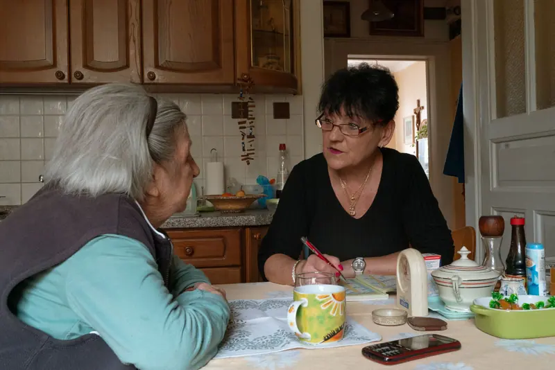 A caregiver and a resident talking over coffee at the kitchen table